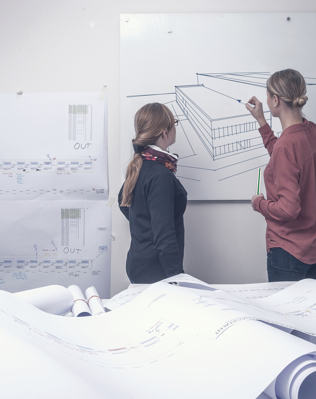 Zwei Architektinnen arbeiten an Bauzeichnungen und besprechen die detaillierte Ausführungsplanung eines Gebäudes.